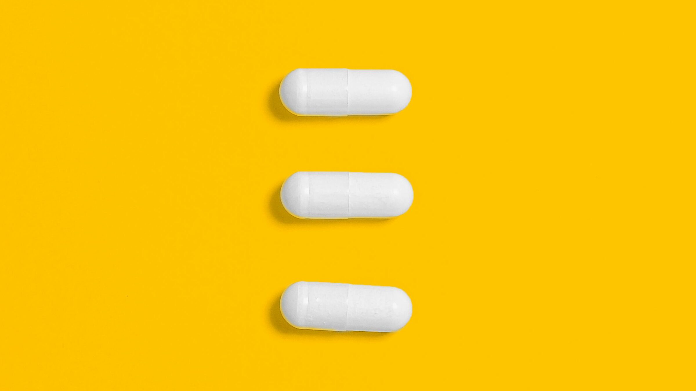 White pills arranged on a vibrant yellow background, emphasizing simplicity and healthcare.
