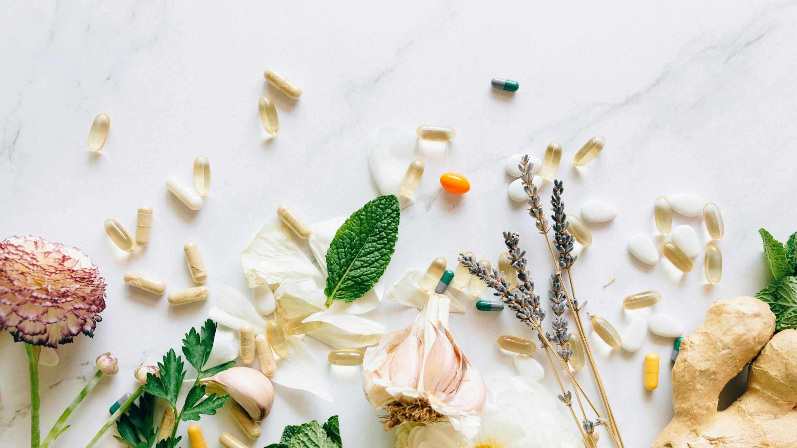 A flatlay of natural herbs, supplements, and flowers on a marble background.