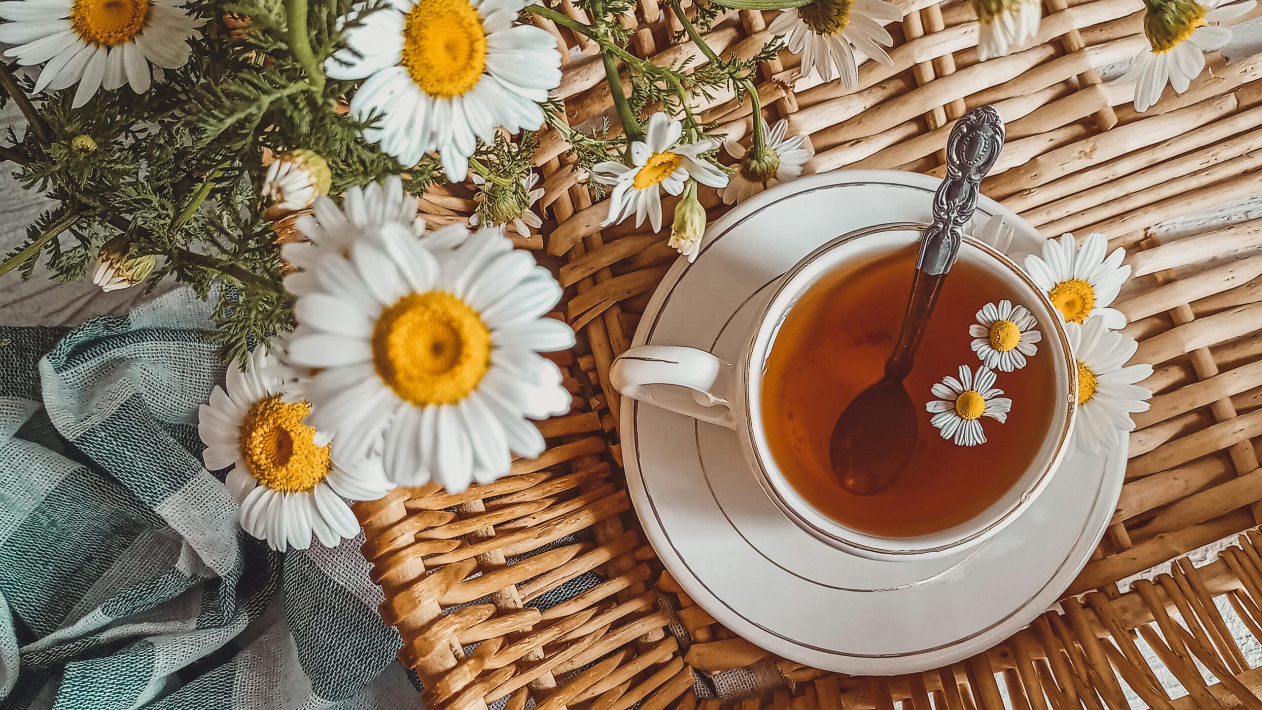 A cozy flatlay featuring chamomile tea in a cup, surrounded by fresh chamomile flowers on a wicker basket.
