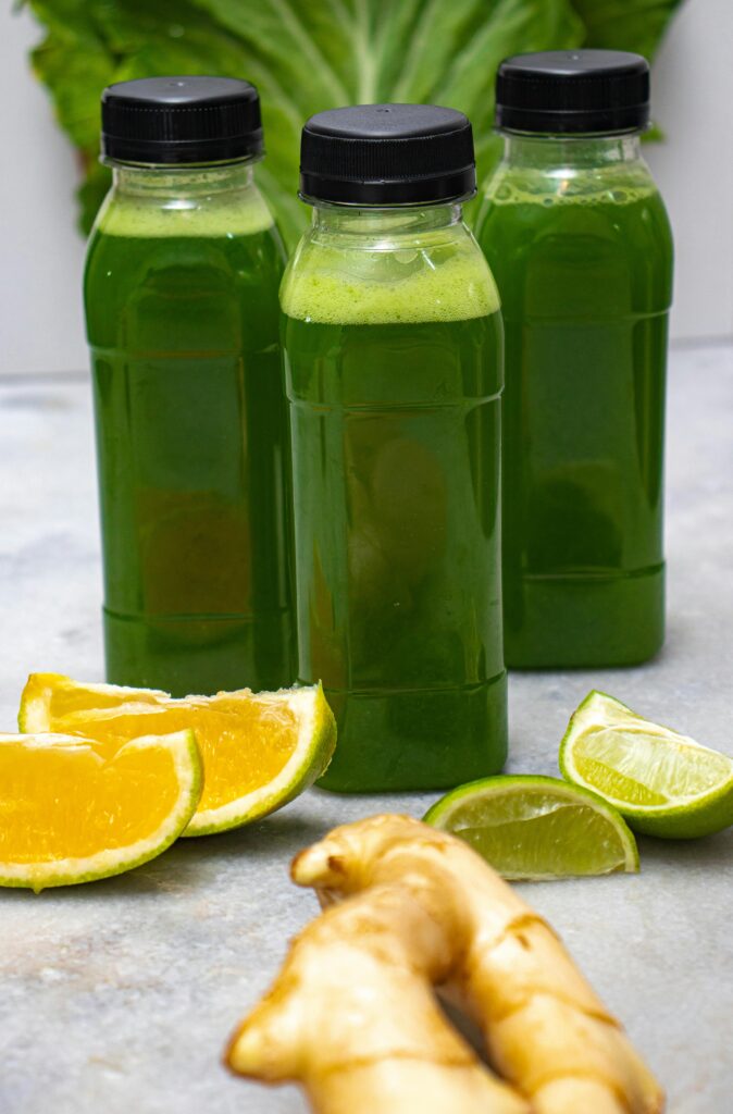 Three bottles of fresh green juice with sliced citrus and ginger displayed on a table.