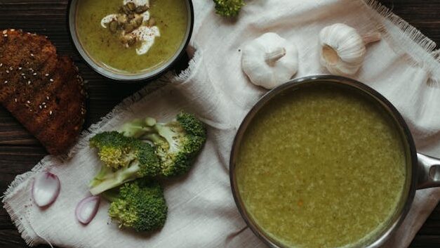 Top view of saucepan with broccoli puree soup on white napkin with garlic and toasted bread slice